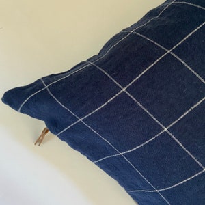 May include: A navy blue pillow with a white grid pattern. The pillow has a zipper closure and a brown zipper pull.