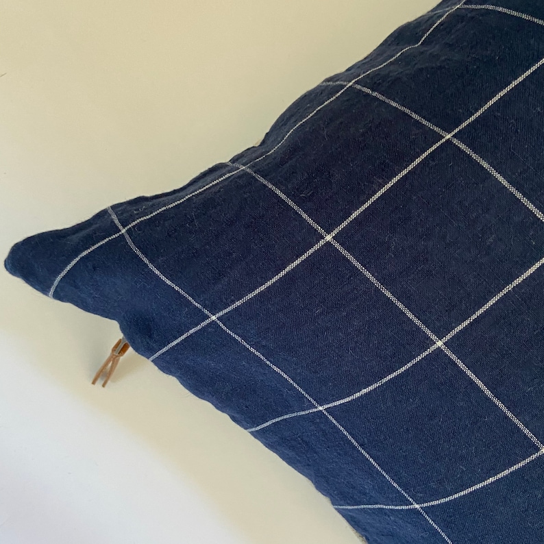 May include: A navy blue pillow with a white grid pattern. The pillow has a zipper closure and a brown zipper pull.