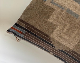Puede incluir: Una almohada de tiro con estampado marrón, azul y rojo con un diseño geométrico. La almohada está hecha de una tela suave y texturizada.