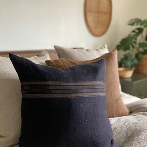 May include: A black throw pillow with brown stripes on a bed with a beige linen duvet cover.