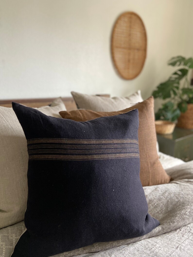 May include: A black throw pillow with brown stripes on a bed with a beige linen duvet cover.