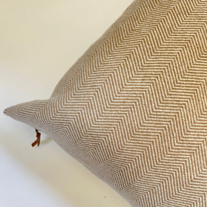May include: A brown and white chevron patterned throw pillow with a brown leather zipper pull.