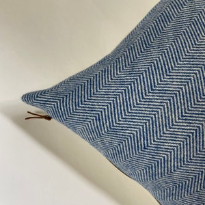 May include: A blue and white chevron patterned throw pillow with a brown leather zipper pull.