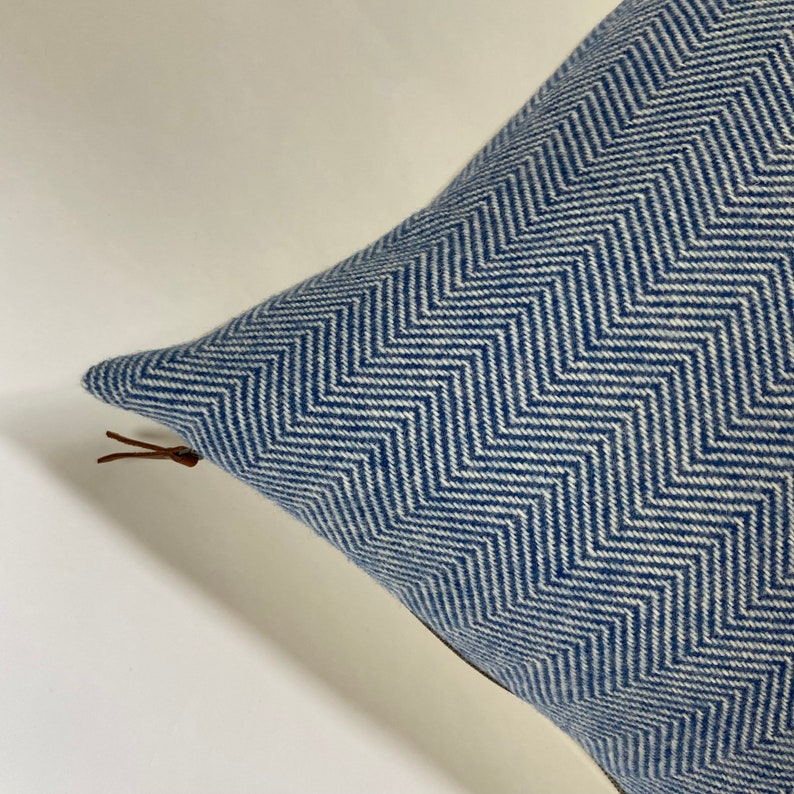 May include: A blue and white chevron patterned throw pillow with a brown leather zipper pull.
