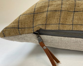 May include: A brown and beige pillow with a blue and white checkered pattern. The pillow has a zipper closure with a brown leather zipper pull that says "MISA".