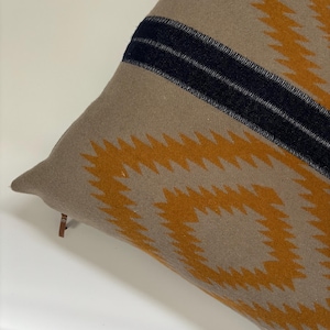 Könnte beinhalten: Ein braunes und beigefarbenes Kissen mit einem geometrischen Muster in Orange- und Schwarztönen. Das Kissen hat einen Reißverschluss und einen Fransenbesatz.