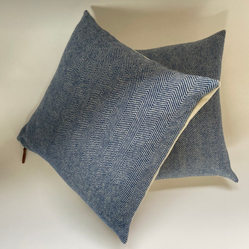 May include: Two blue and white chevron patterned throw pillows with a white border. The pillows are stacked on top of each other.