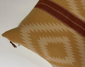 Puede incluir: Una almohada de sofá de color amarillo mostaza con un patrón geométrico y una franja roja en la parte superior. La almohada tiene una cremallera.