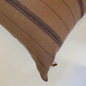 May include: A brown and black striped throw pillow with a brown leather tassel.