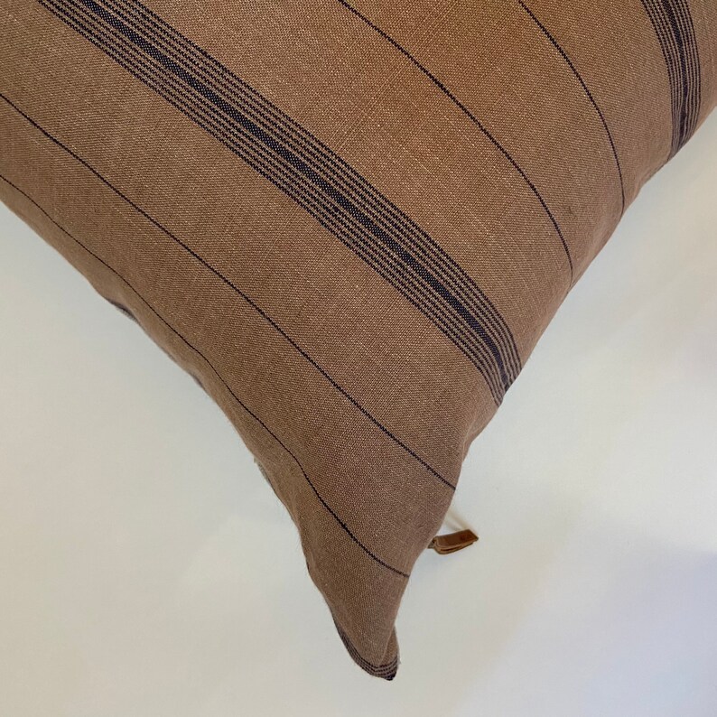 May include: A brown and black striped throw pillow with a brown leather tassel.