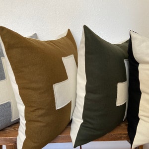 May include: Four decorative throw pillows with a white cross design. The pillows are made of different fabrics in gray, brown, green, and black.