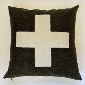 Puede incluir: Una almohada verde con un diseño de cruz suiza blanca. La almohada está hecha de un material suave y peludo.