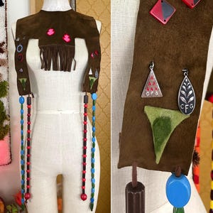 Puede incluir: Un chaleco de ante marrón con flecos, cuentas y bordados coloridos. El chaleco tiene dos correas largas con cuentas rojas y azules. El chaleco está decorado con pequeñas formas geométricas coloridas y un diseño de hoja verde.