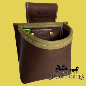 May include: A brown leather shotgun shell holder with a tan leather trim and a Stagecoach Leather logo. The holder has a belt loop on the back.