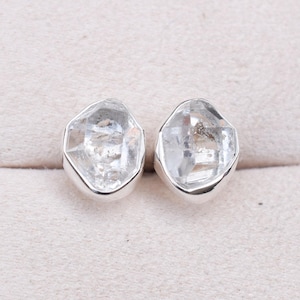 May include: A pair of silver earrings with clear, faceted, geometric gemstones. The earrings are set in a simple, modern style.