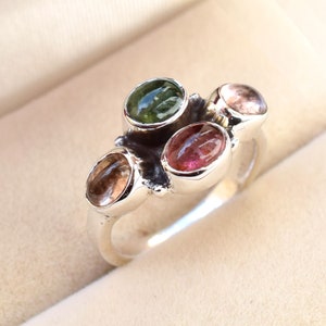 Può includere: Un anello d'argento con quattro pietre ovali. Le pietre sono verdi, rosa e marroni.
