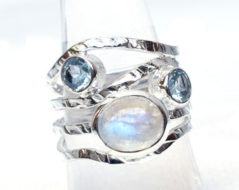 Könnte beinhalten: Ein silberner Ring mit einem großen, weißen Mondstein und zwei kleineren, hellblauen Edelsteinen. Der Ring hat eine strukturierte, gehämmerte Band.