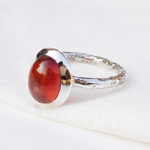 May include: A silver ring with a textured band and a large, round, red gemstone.