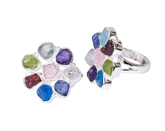 May include: Two silver rings with clusters of colorful gemstones. The gemstones are various shapes and colors, including blue, purple, pink, green, and red. The rings are set against a white background.