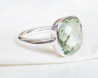May include: A silver ring with a large, light green gemstone. The gemstone is a cushion cut and has a faceted design.