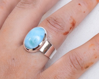 Könnte beinhalten: Ein silberner Ring mit einem großen, ovalen, hellblauen Edelstein. Der Edelstein ist in einem polierten Silberband gefasst. Der Ring wird an einem Finger gezeigt. Das Design ist schlicht.