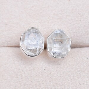 May include: A pair of silver earrings with clear, faceted crystal stones. The stones are set in a simple, geometric shape.