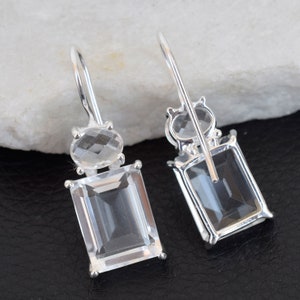 May include: A pair of silver dangle earrings with clear quartz gemstones. The earrings feature a rectangular shaped stone and a smaller oval shaped stone.