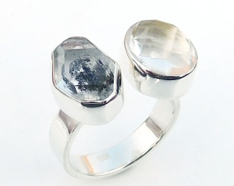 Può includere: Un anello d'argento con due pietre di quarzo trasparenti. Le pietre sono incastonate in una montatura a castone e sono collegate da una fascia d'argento.
