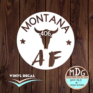 May include: White vinyl decal with a bull skull, the text "MONTANA 406 AF" and two stars. The decal is on a brown wooden background.