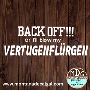 May include: White vinyl decal with the text "BACK OFF!!! or I'll blow my VERTUGENFLÜRGEN" on a wood background. The decal is available from Montana Decal Gal, a company that sells decals and stickers.