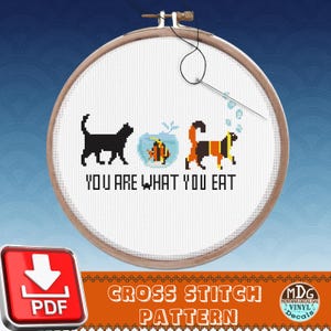 May include: A cross-stitch pattern in a wooden hoop features a black cat, a fish in a bowl, and a dog with the text "YOU ARE WHAT YOU EAT." The design includes a needle and thread, with the words "CROSS STITCH PATTERN" at the bottom.