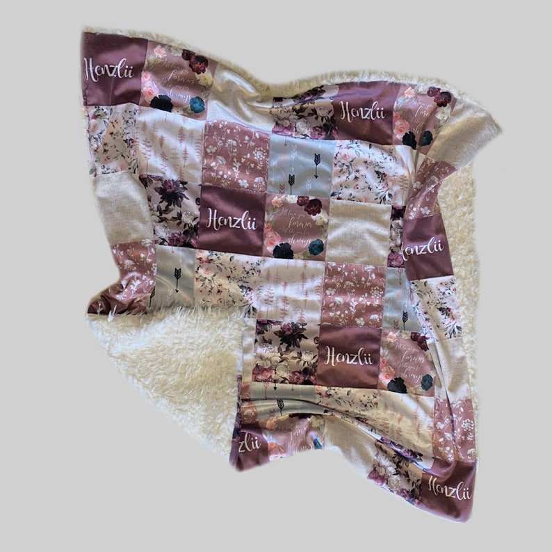 Puede incluir: Una manta suave y mullida para beb&eacute; con un dise&ntilde;o de patchwork que presenta patrones florales y el nombre "Henzli" repetido en toda la superficie. La manta tiene un respaldo de sherpa blanco.