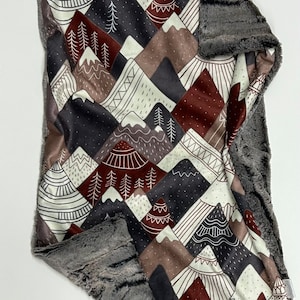 Puede incluir: Una manta suave y mullida con un diseño de montaña y bosque. El lado delantero presenta un fondo blanco con montañas marrones, rojas y grises, árboles y patrones geométricos. El lado trasero es un tejido de felpa gris sólido.