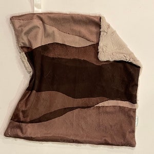 Puede incluir: Una manta de felpa suave de color marrón y beige con un patrón ondulado. Un lado de la manta es de tela de felpa, y el otro lado es de piel sintética.