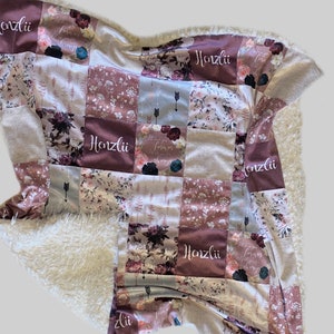 Puede incluir: Una manta de beb&eacute; de patchwork con un respaldo de sherpa blanco suave. La manta est&aacute; hecha de varias telas con patrones florales y el nombre "Honzlii" bordado en varios de los cuadrados.