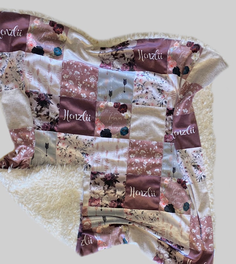 Puede incluir: Una manta de beb&eacute; de patchwork con un respaldo de sherpa blanco suave. La manta est&aacute; hecha de varias telas con patrones florales y el nombre "Honzlii" bordado en varios de los cuadrados.