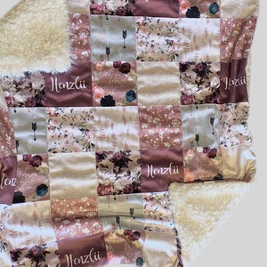Puede incluir: Una manta de beb&eacute; de patchwork con un respaldo de sherpa blanco suave. La manta presenta un patr&oacute;n floral con un esquema de color rosa y marr&oacute;n. El nombre "Henzli" est&aacute; bordado en varios de los cuadrados.
