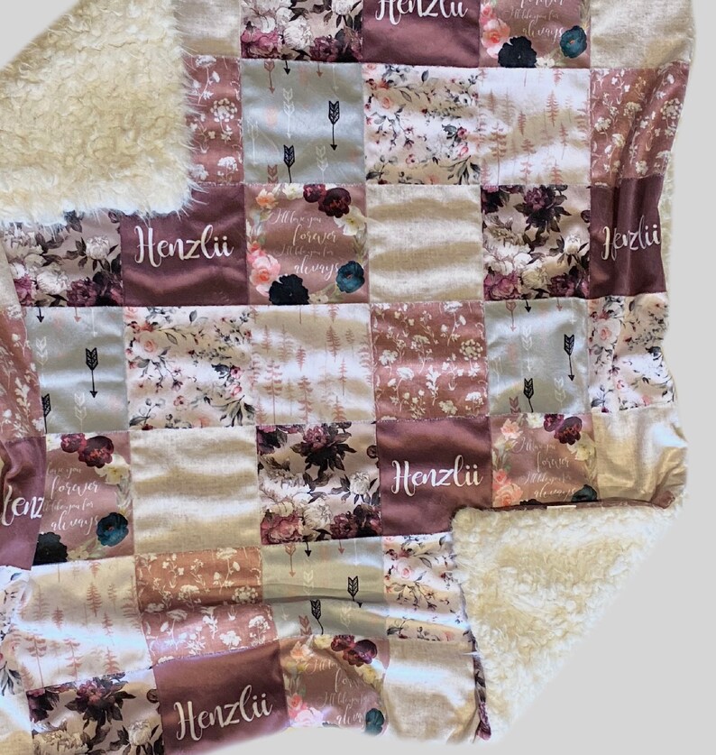 Puede incluir: Una manta de beb&eacute; de patchwork con un respaldo de sherpa blanco suave. La manta presenta un patr&oacute;n floral con un esquema de color rosa y marr&oacute;n. El nombre "Henzli" est&aacute; bordado en varios de los cuadrados.