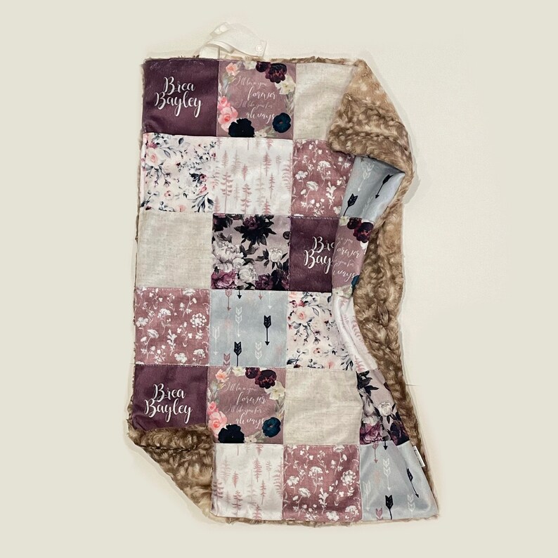Puede incluir: Una manta suave y mullida para beb&eacute; con un dise&ntilde;o de patchwork que presenta patrones florales, flechas y el nombre "Brea Bayley" en una fuente cursiva. La manta est&aacute; hecha de una combinaci&oacute;n de telas, incluyendo un material suave y peludo en un lado y una tela de algod&oacute;n en el otro.