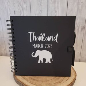 May include: Black scrapbook with a white elephant silhouette and the text "Thailand March 2023".