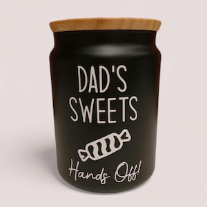 May include: Black ceramic jar with a wooden lid. The jar has white text that says "Dad's Sweets Hands Off!" and a white candy illustration.