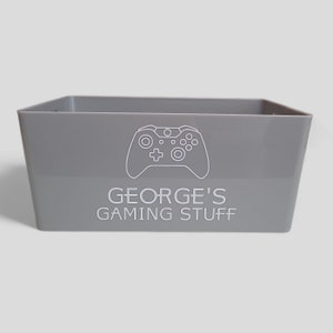 May include: A grey plastic storage box with a white outline of a video game controller and the text "GEORGE'S GAMING STUFF" on the front.