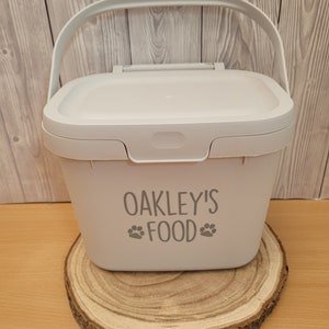 May include: A white plastic container with a handle and a lid. The container has the text "OAKLEY'S FOOD" with paw prints on either side of the word "FOOD".