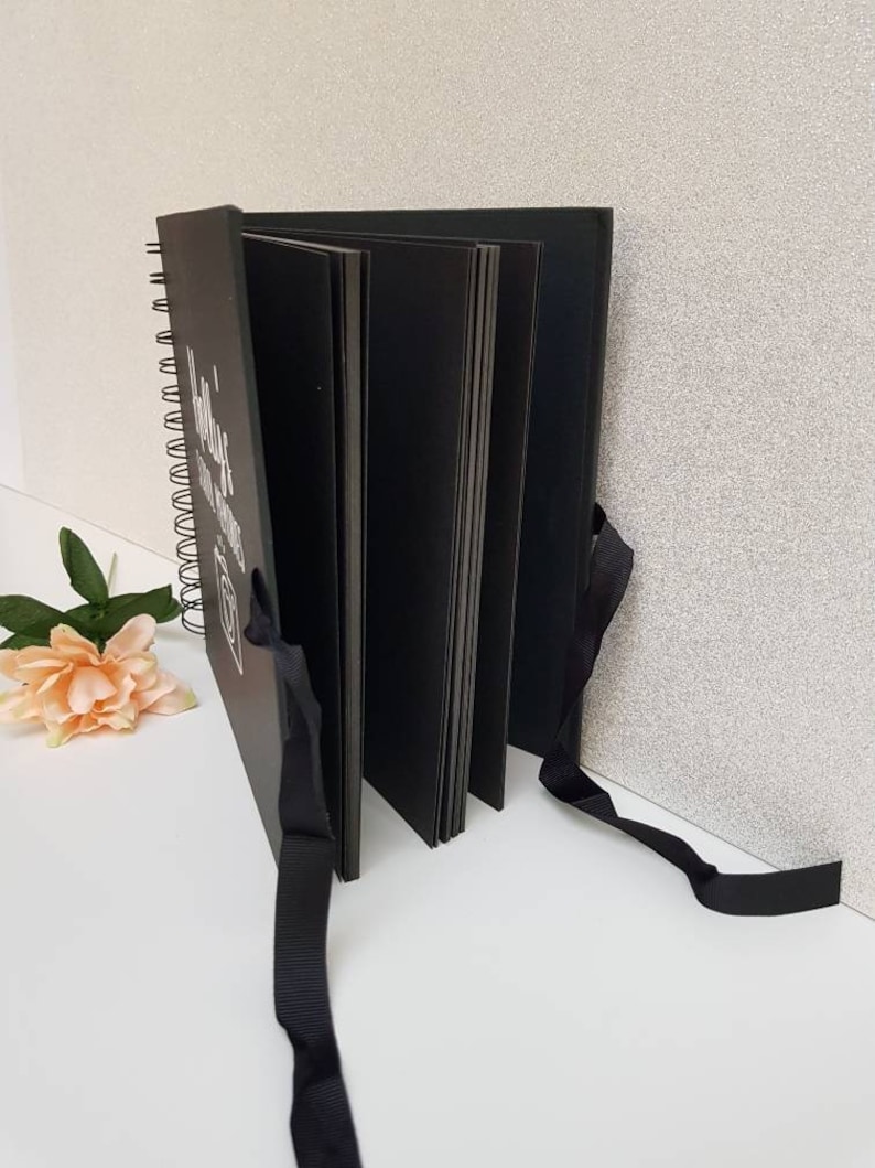 May include: Black spiral bound photo album with black ribbon ties. The cover has white text that reads "Hello, you are amazing".