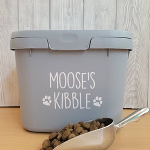 May include: Gray plastic pet food container with a white label that says "Moose's Kibble" with paw prints. A silver scoop is filled with brown kibble.
