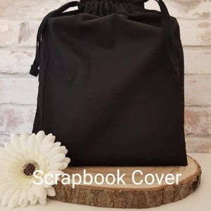 May include: Black drawstring bag with a gathered top, sitting on a wooden round slice. The bag is labeled "Scrapbook Cover".