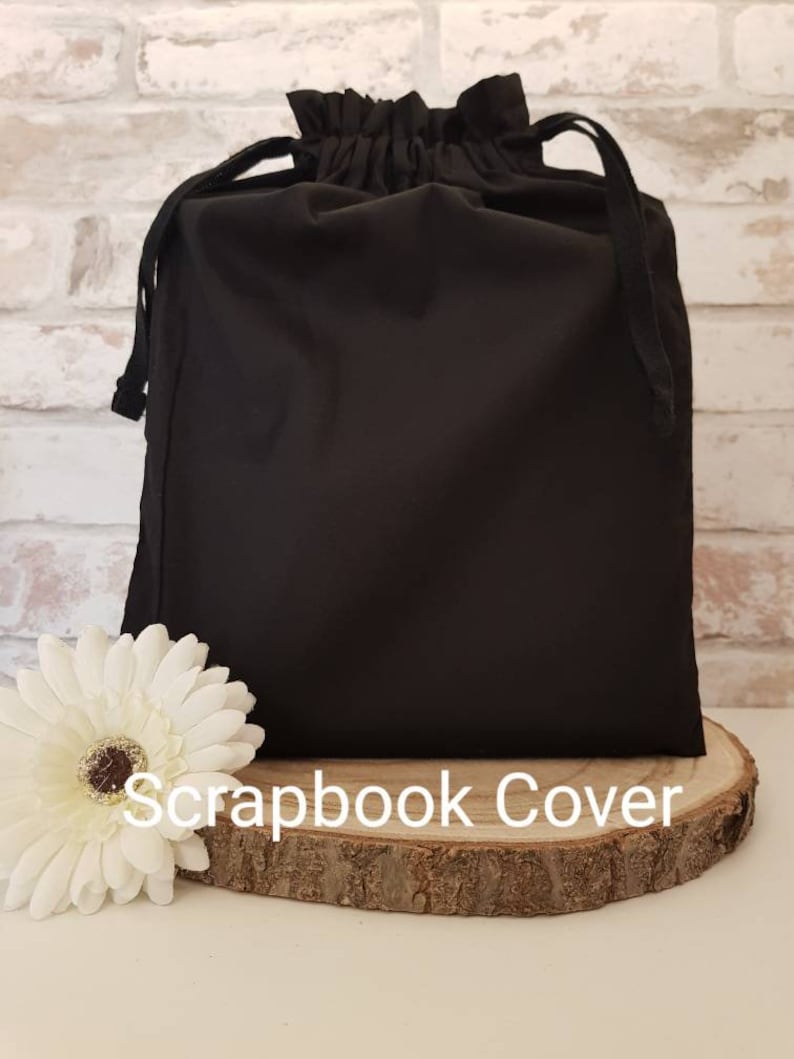 May include: Black drawstring bag with a gathered top, sitting on a wooden round slice. The bag is labeled "Scrapbook Cover".