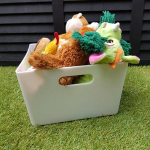 Op de afbeelding: Een witte plastic opbergbox met een handvat, gevuld met verschillende pluche speelgoed, waaronder een groene en roze draak, een bruine beer en een bruine en witte aap.