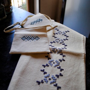 May include: Three white fabric bags with blue embroidered designs. The bags are folded and stacked on a dark surface.