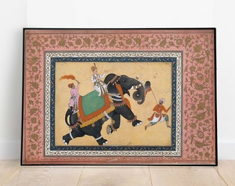 May include: A framed painting depicting a black elephant with a rider and a handler. The elephant is adorned with a green and gold saddle cloth. The painting is set against a pink background with gold floral designs.